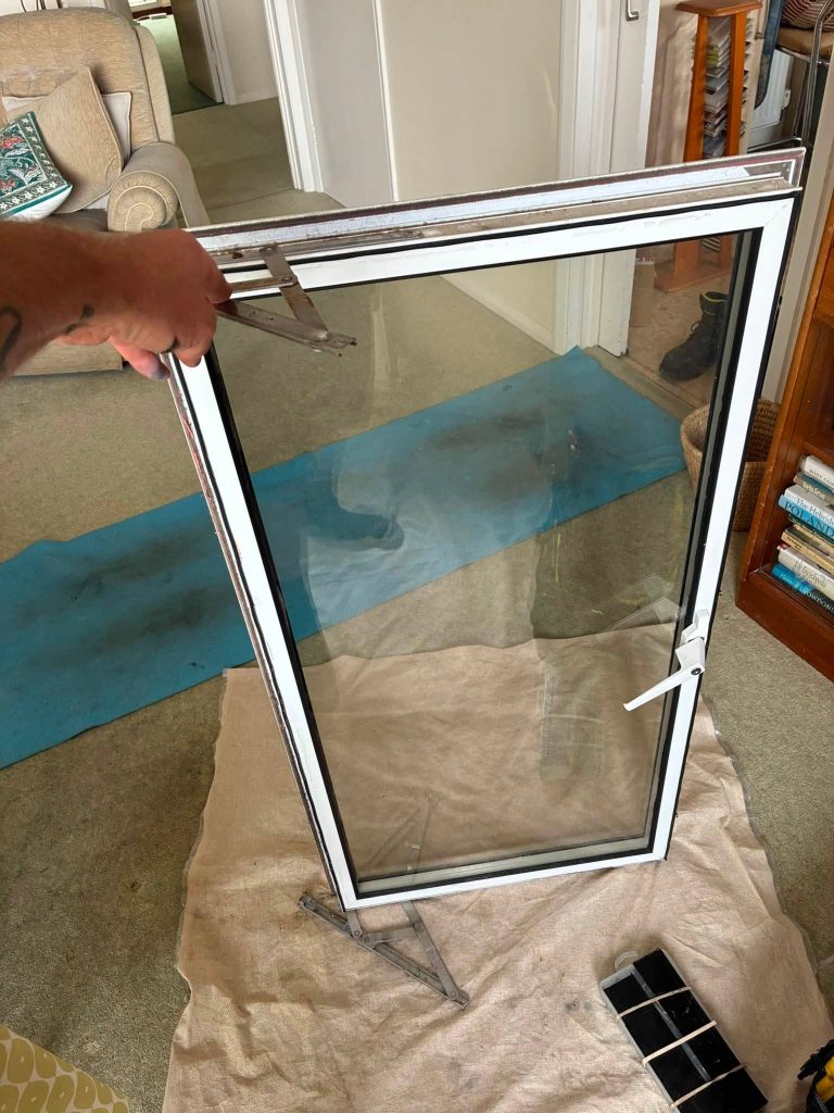 ASL Locksmiths technician holding a removed uPVC window sash showing corroded metal friction hinges in Eastbourne.