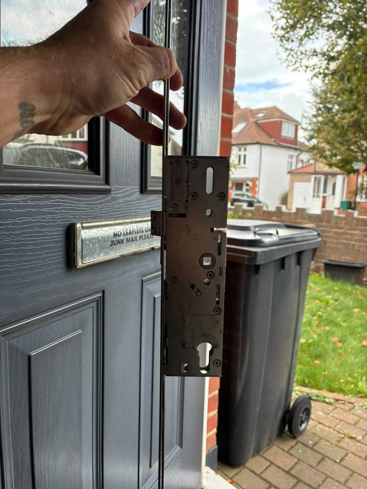 Locksmith holding up a new multipoint lock gearbox mechanism in front of an open grey composite door in Hellingly.
